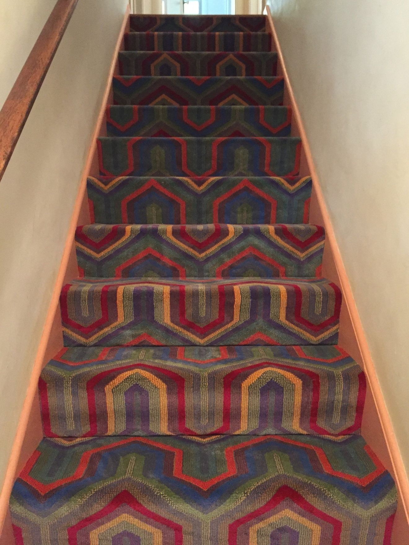 Carpeted staircase with red, blue, and gold geometric pattern and wooden handrails