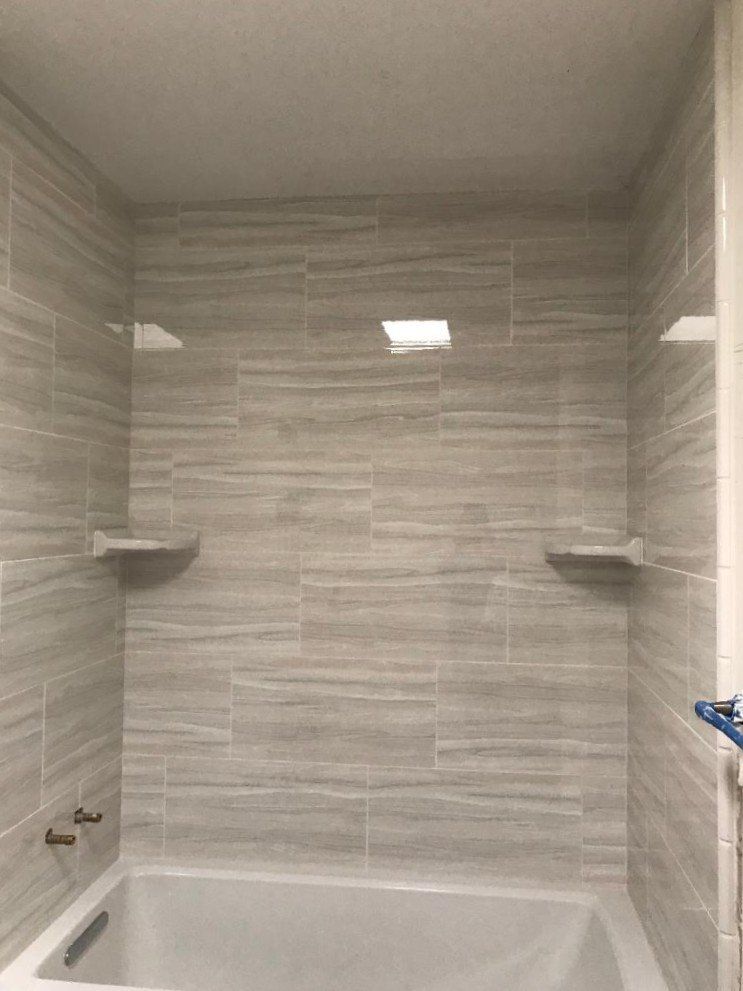 Small tiled bathtub alcove with gray walls, white tub, and two corner shelves under recessed lights