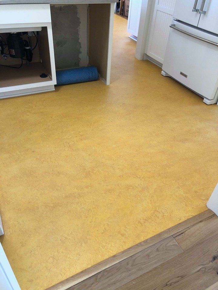 Kitchen flooring installation showing a bright yellow linoleum floor with exposed cabinet
