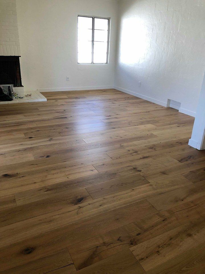 Empty living room with natural light oak hardwood flooring, white walls, and a brick fireplace.