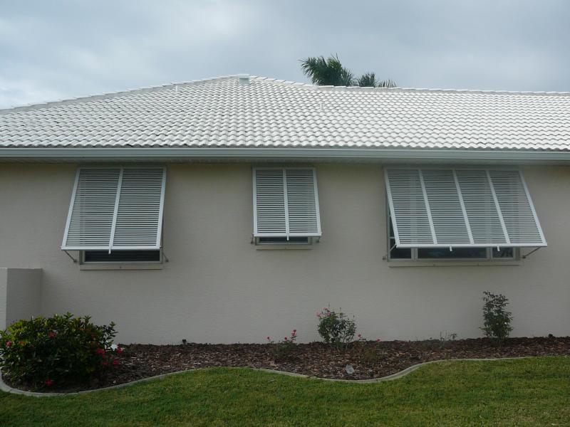 White house with three windows featuring open, white, louvered shutters.