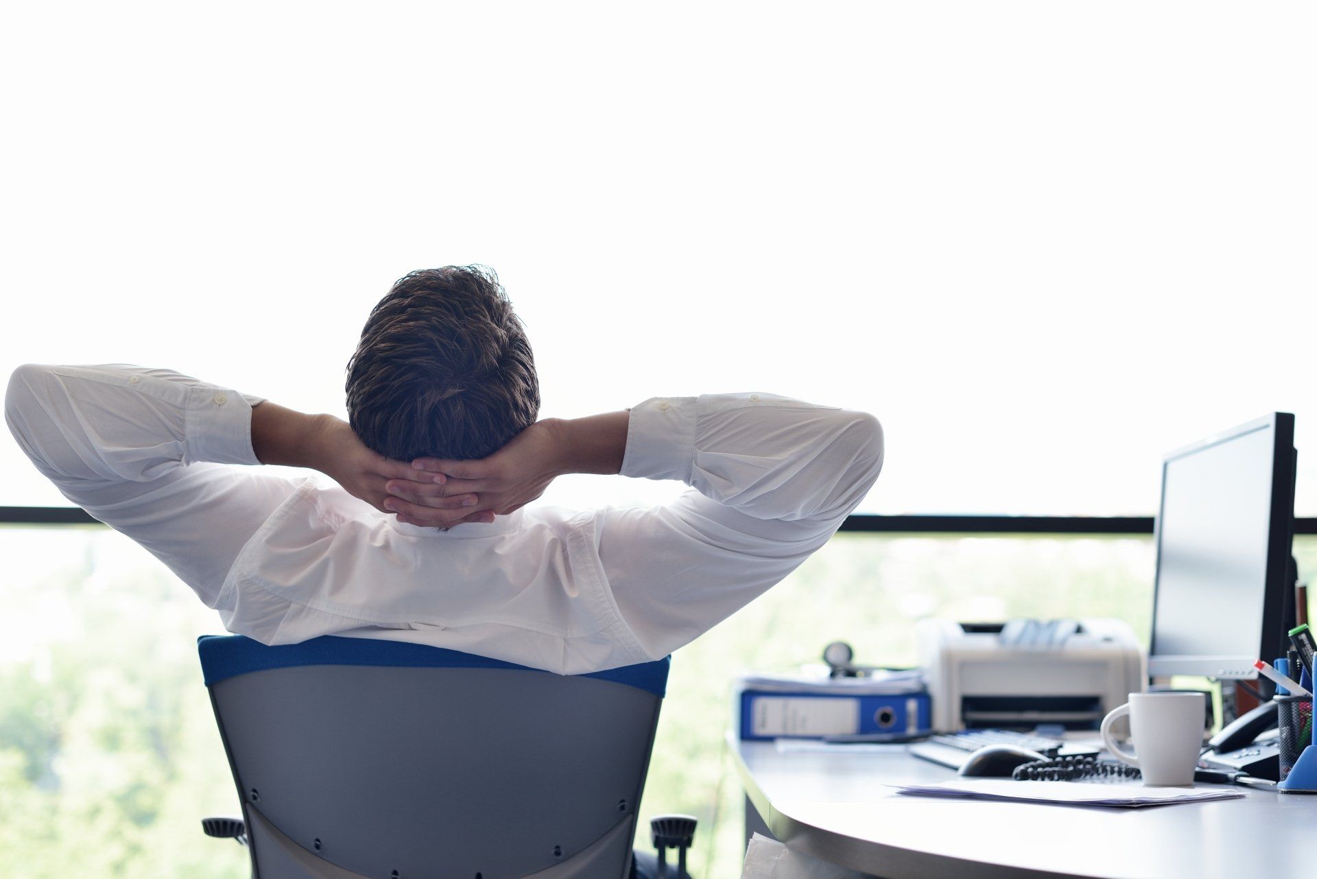 A man is sitting in an office chair with his hands behind his head.
