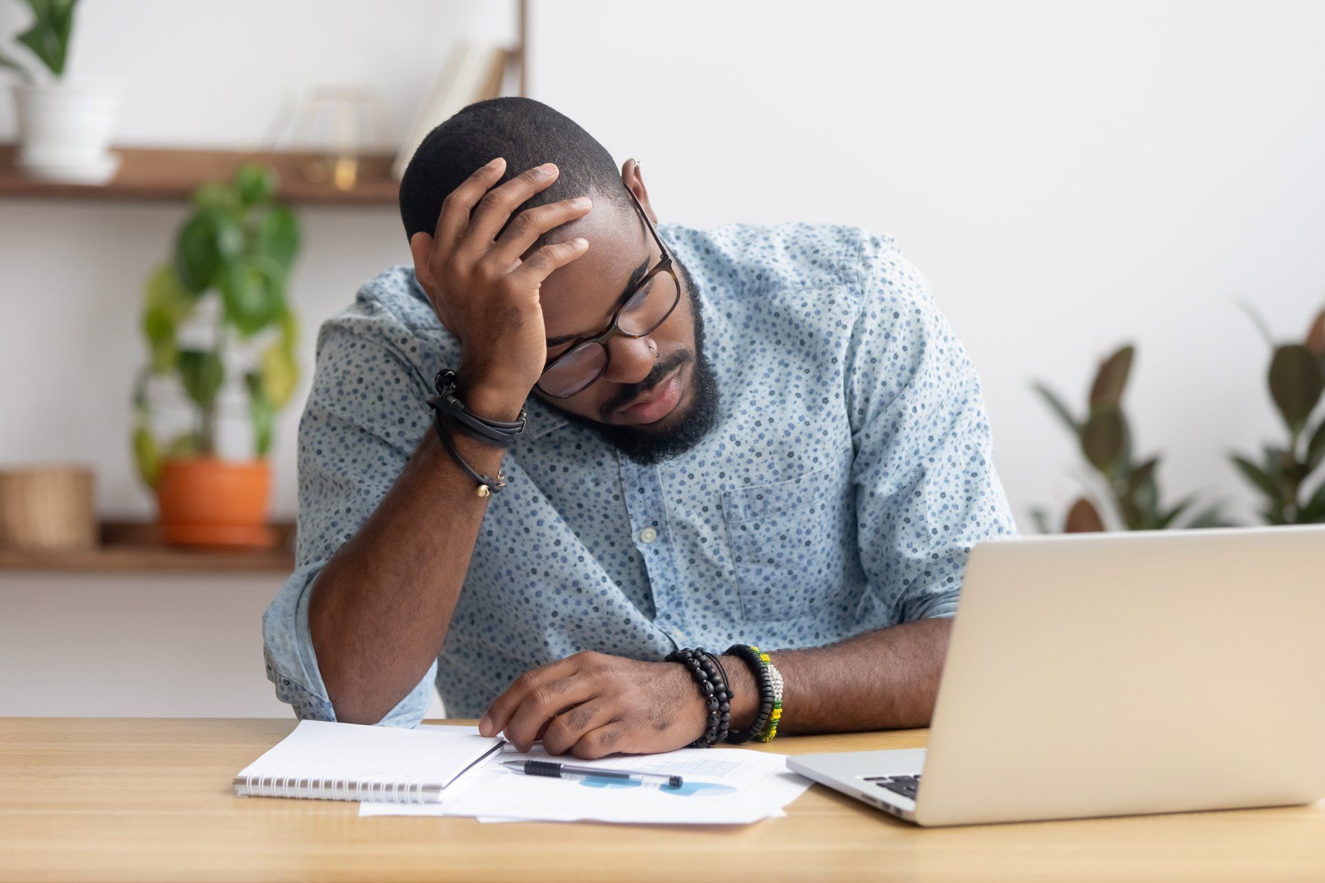 A man is sitting at a desk with a laptop and holding his head.