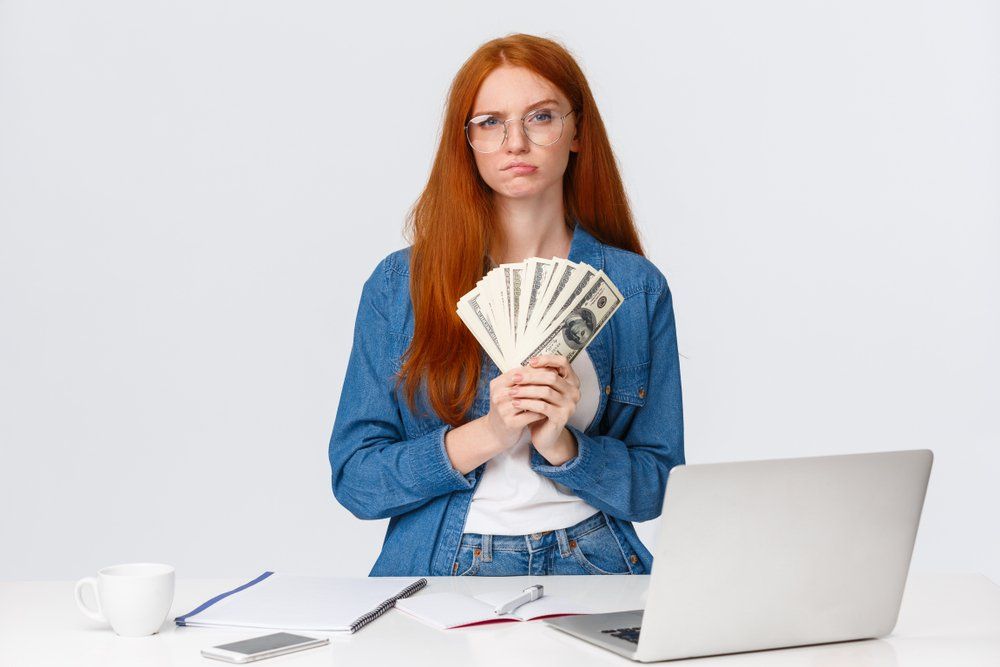 A woman is sitting at a desk holding a fan of money.