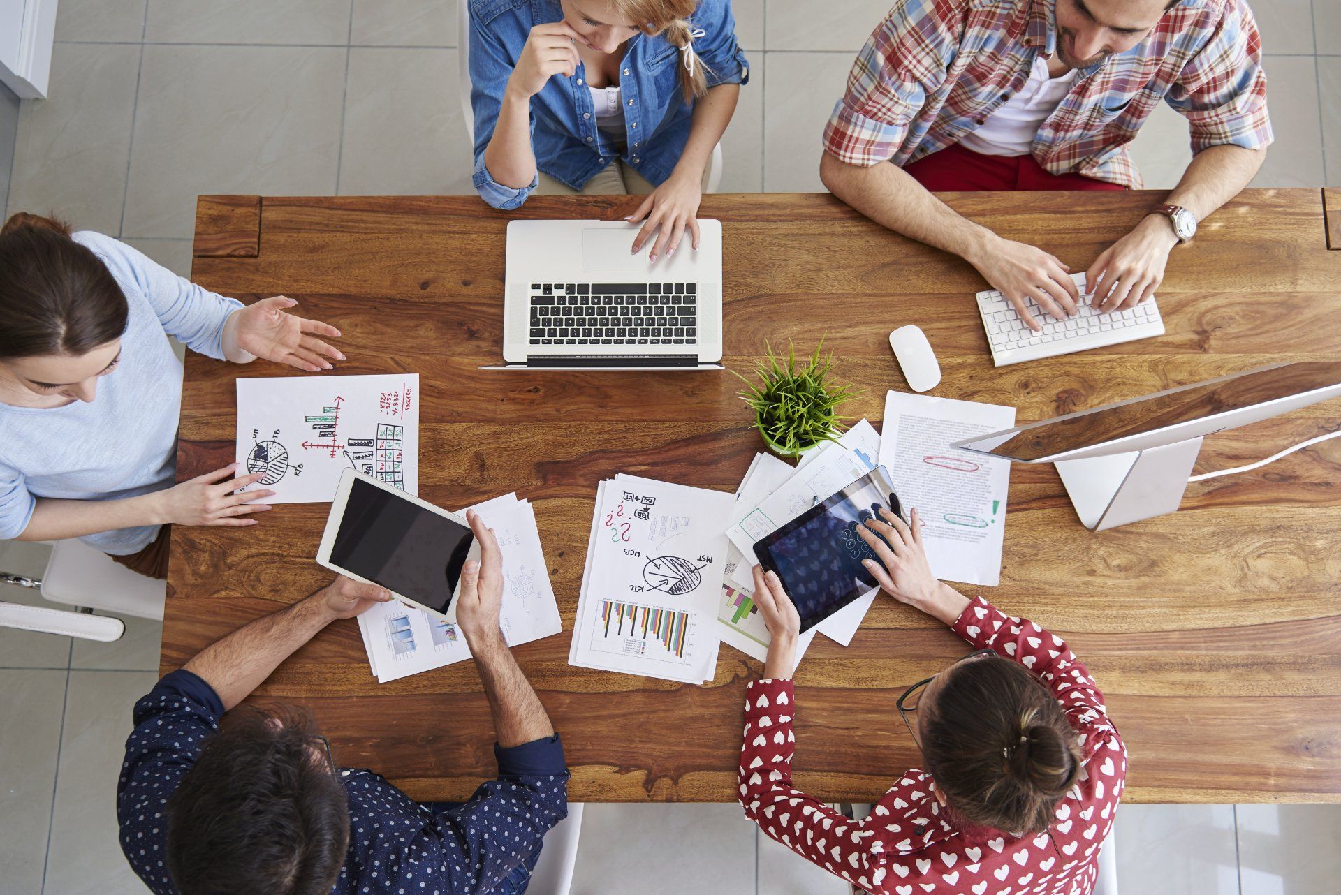 A group of people are sitting around a wooden table with laptops and tablets.