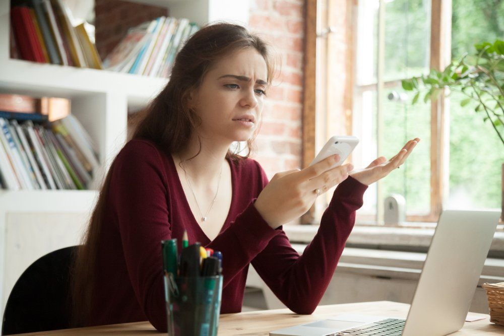 A woman is sitting at a desk looking at her cell phone.