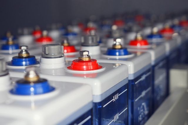File di batterie industriali al piombo-acido con cappucci terminali rossi e blu, disposte su una scaffalatura.