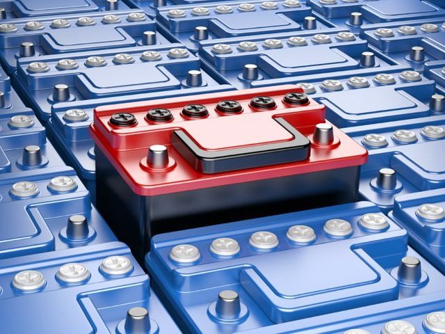 Una batteria per auto di colore rosso acceso, posizionata al centro di una griglia composta da numerose batterie blu identiche.