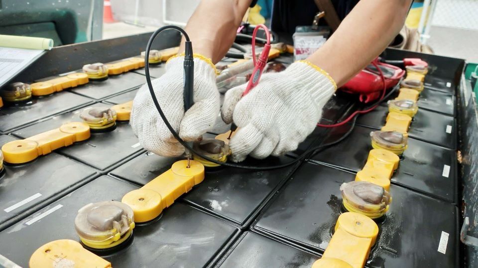 Un tecnico con indosso guanti da lavoro bianchi utilizza un multimetro per testare la tensione delle celle di una batteria industriale.
