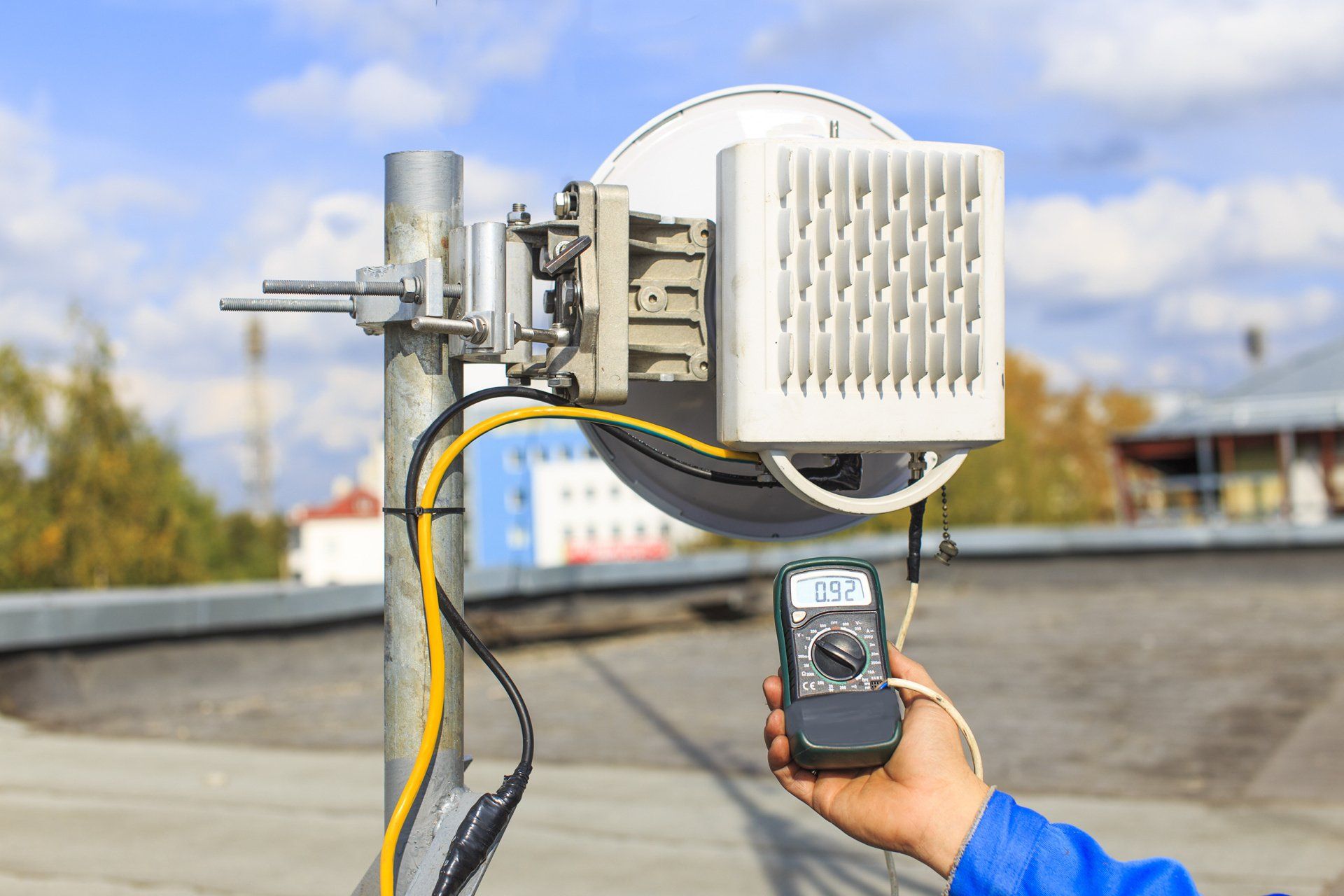 A person is holding a digital multimeter in front of a satellite dish.