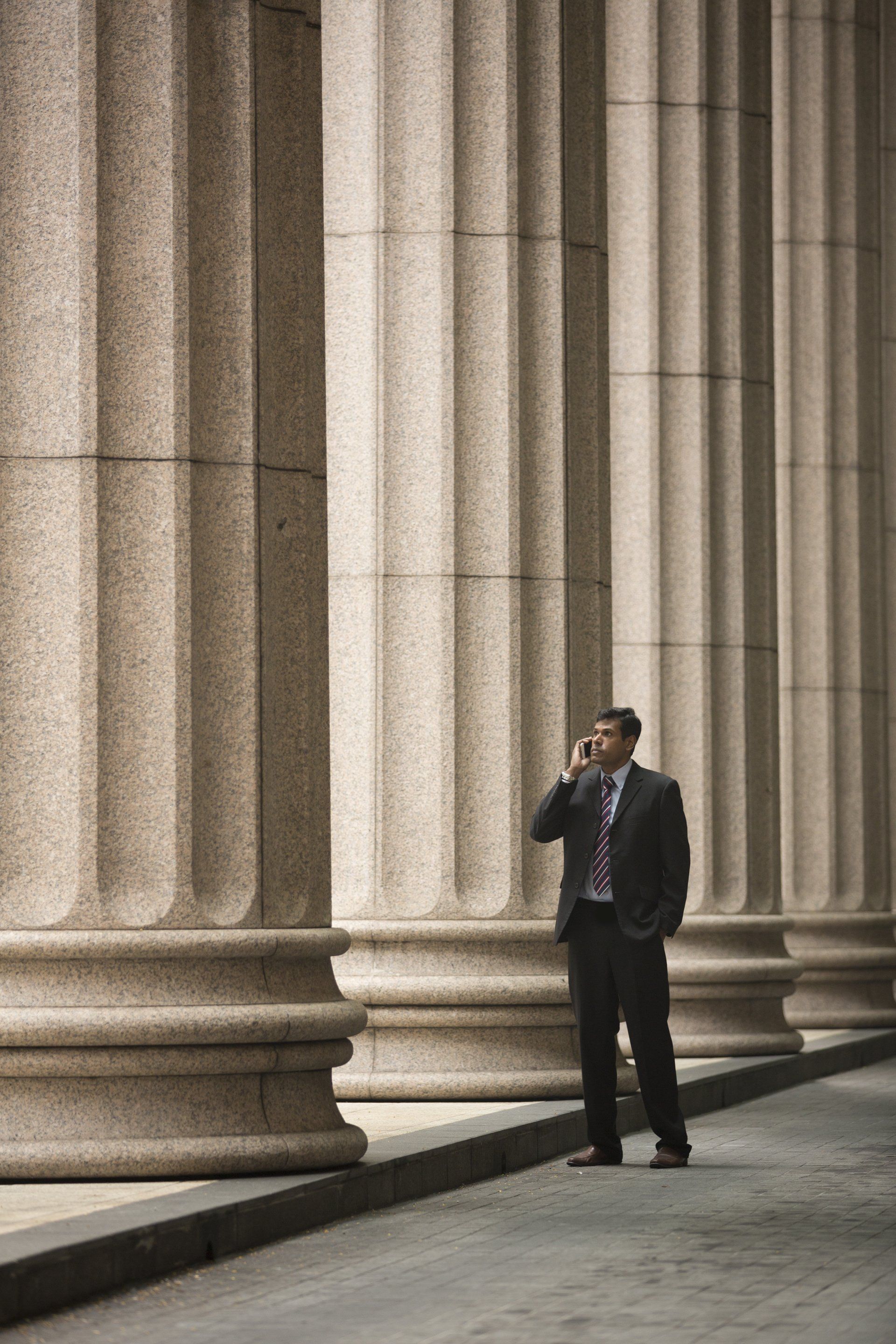 A man in a suit is standing in front of a building talking on a cell phone.