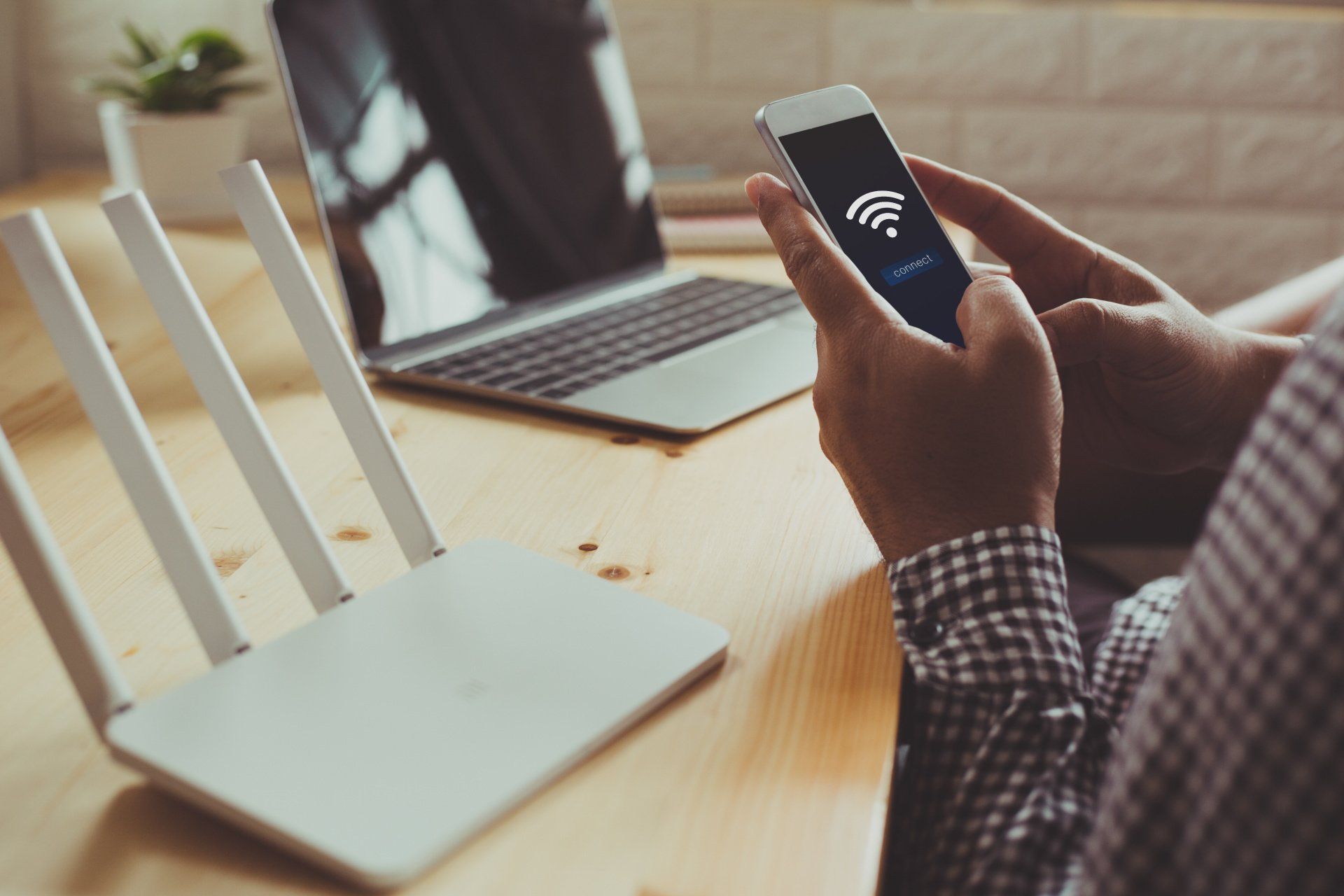 A person is holding a cell phone in front of a laptop and a router.