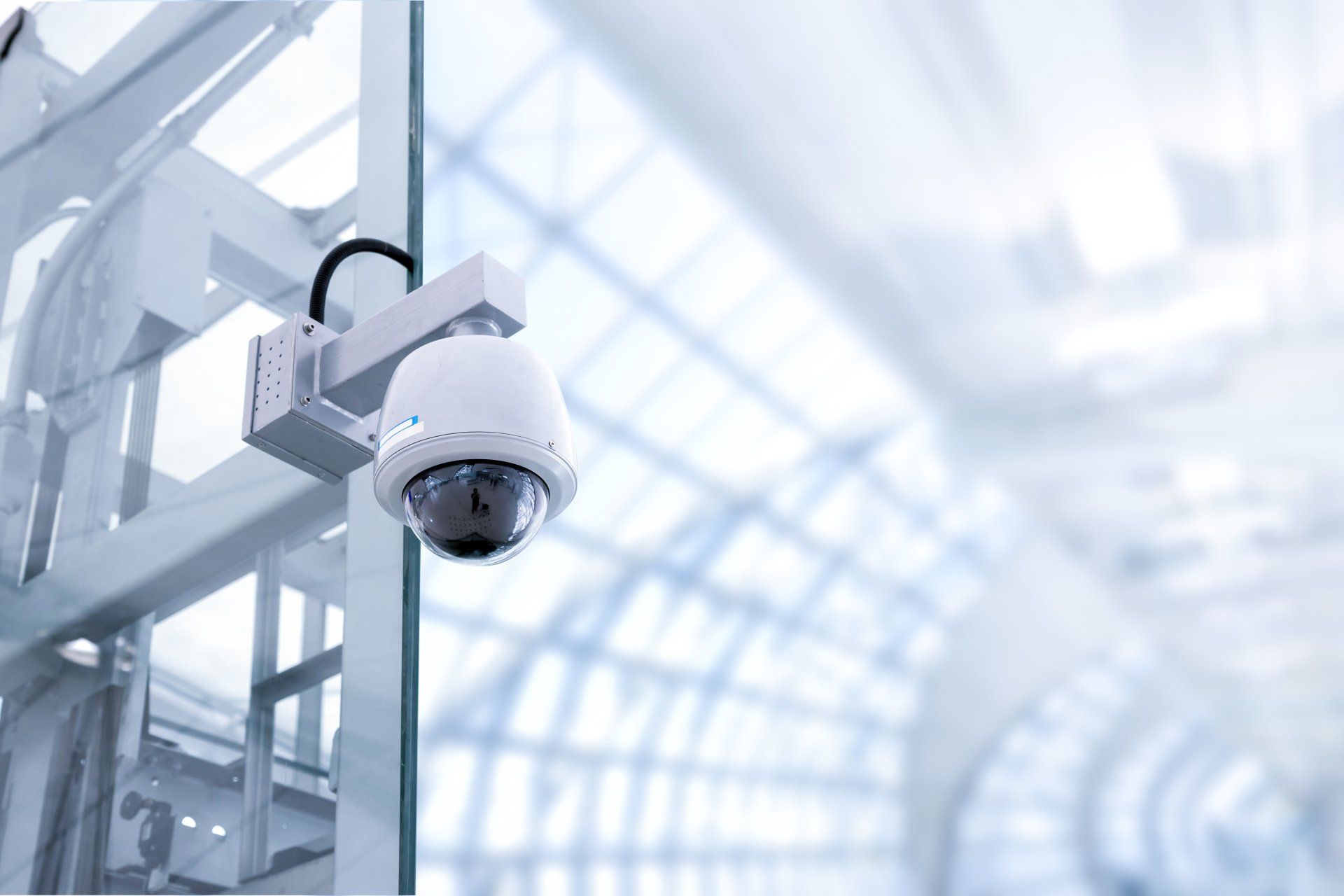 A security camera hanging from a glass wall in a building.
