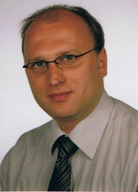 A man wearing glasses and a tie looks at the camera