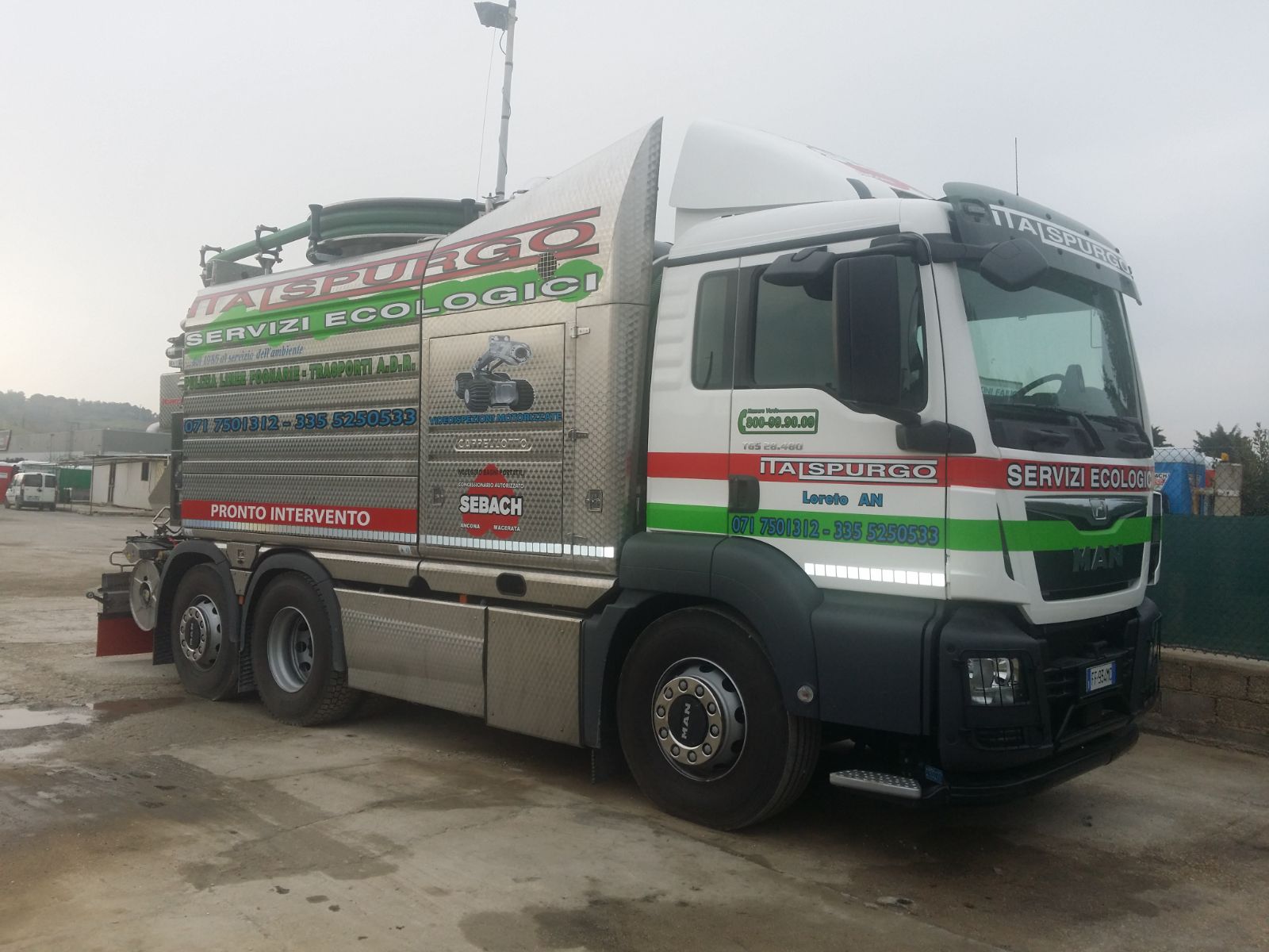 Un camion da carico bianco decorato è parcheggiato sul ciglio di una strada bagnata in una zona industriale nebbiosa.