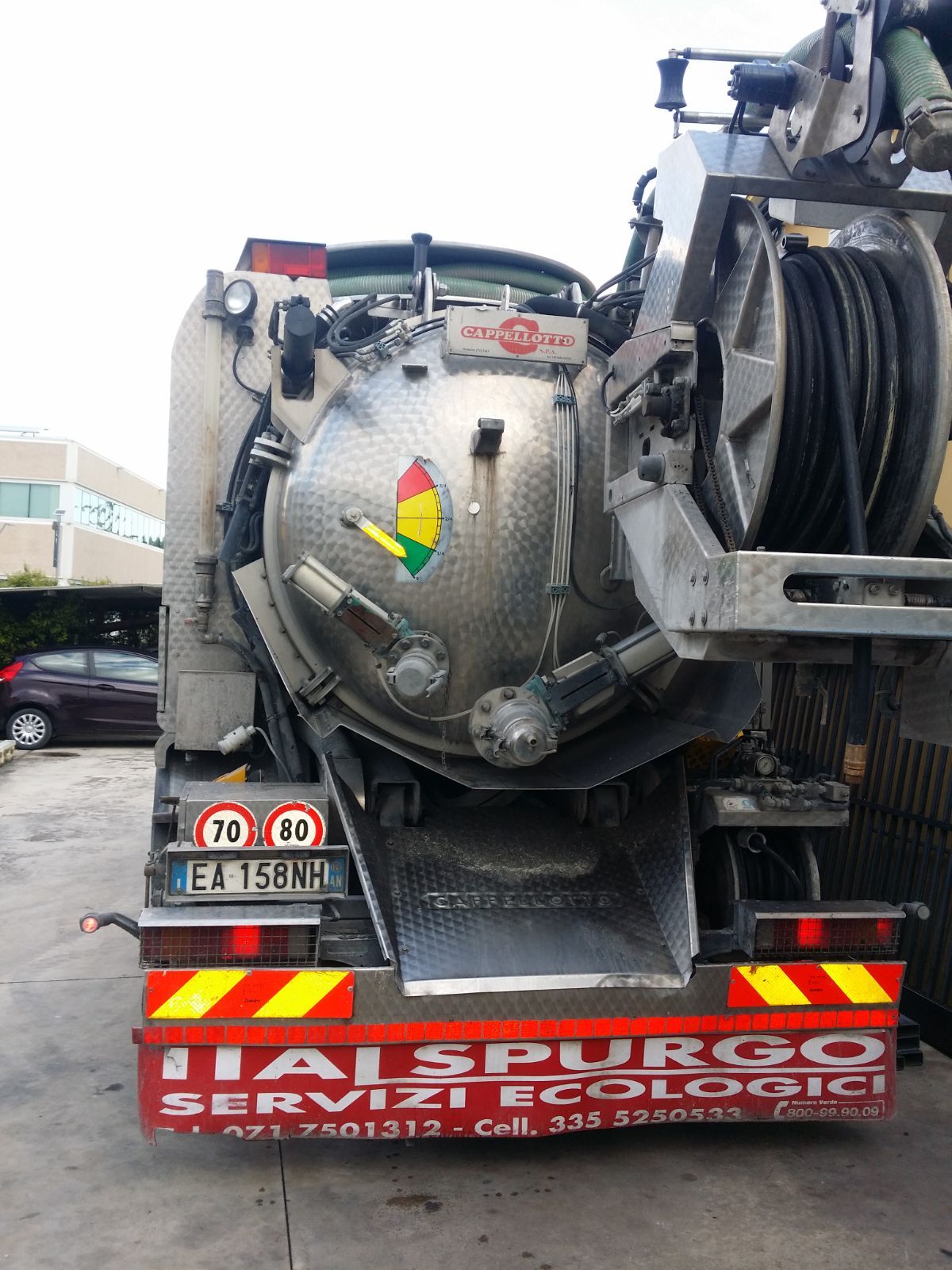 Parte posteriore di un camion aspiratore rosso e argento con avvolgitubo e insegna di servizio italiana in un parcheggio.