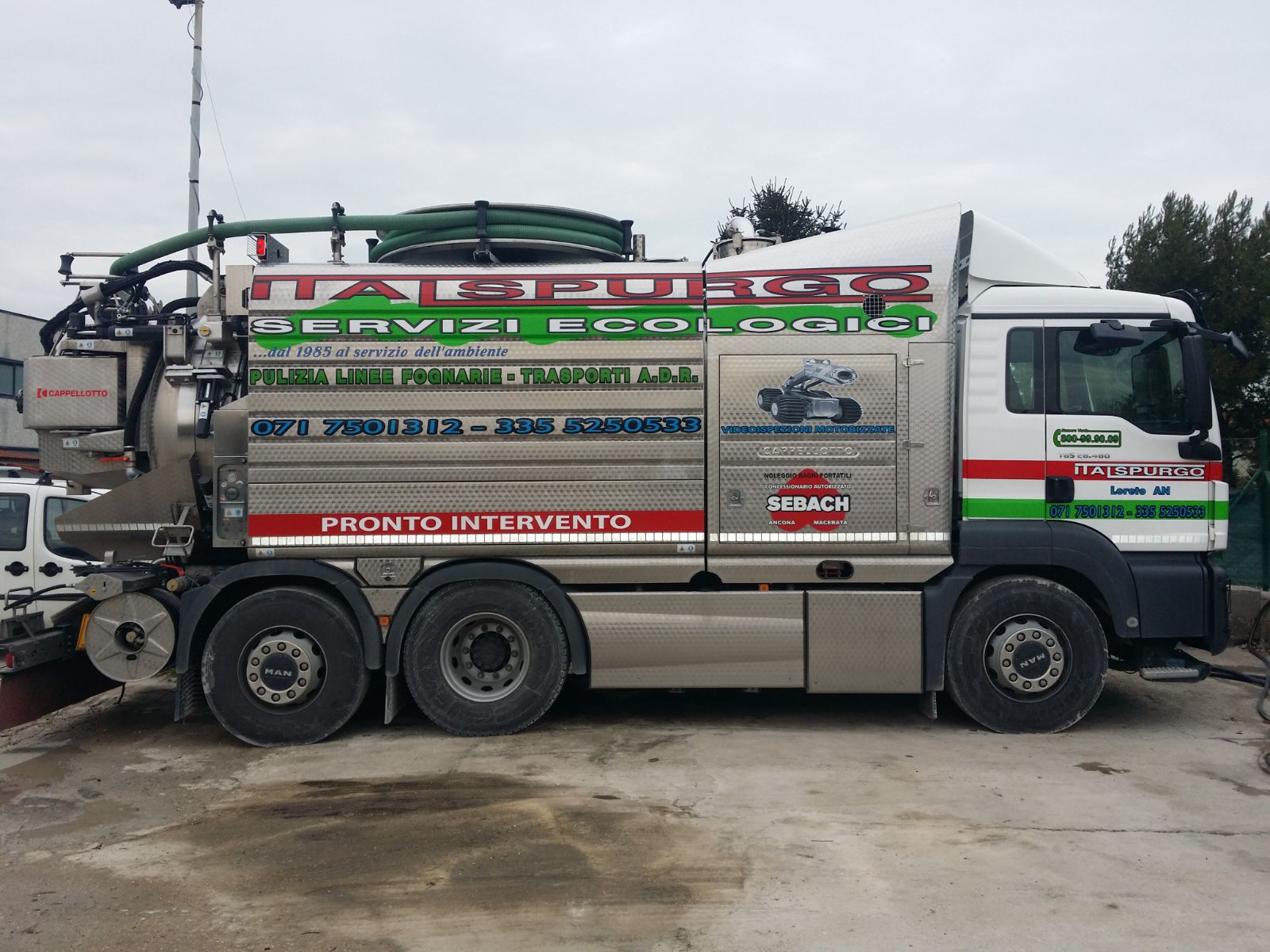Un camion di servizio rosso e bianco con tubi e attrezzature parcheggiato su un terreno bagnato.