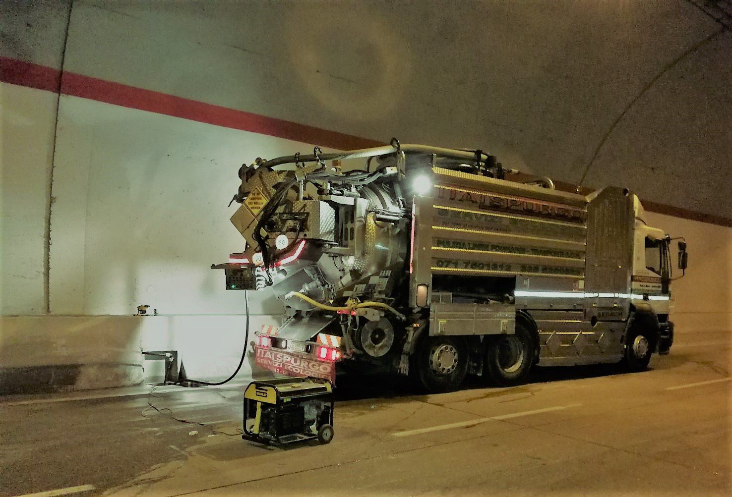 Camion della spazzatura all'interno di una galleria, la parte posteriore danneggiata o esposta, con detriti e attrezzature nelle vicinanze.