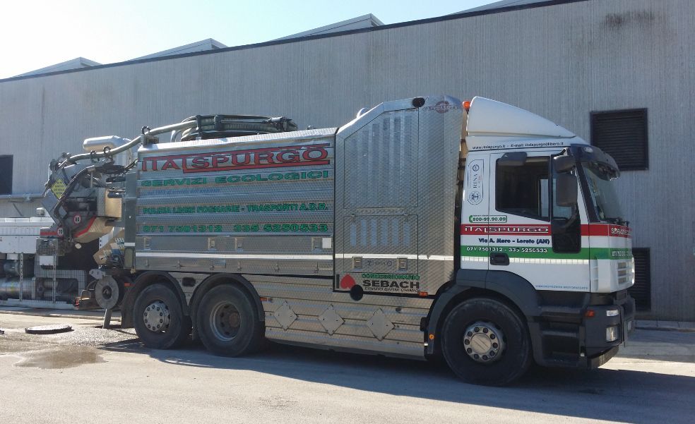 Un camion ribaltabile argentato con pannelli laterali colorati, parcheggiato fuori da un magazzino sotto la luce del sole.