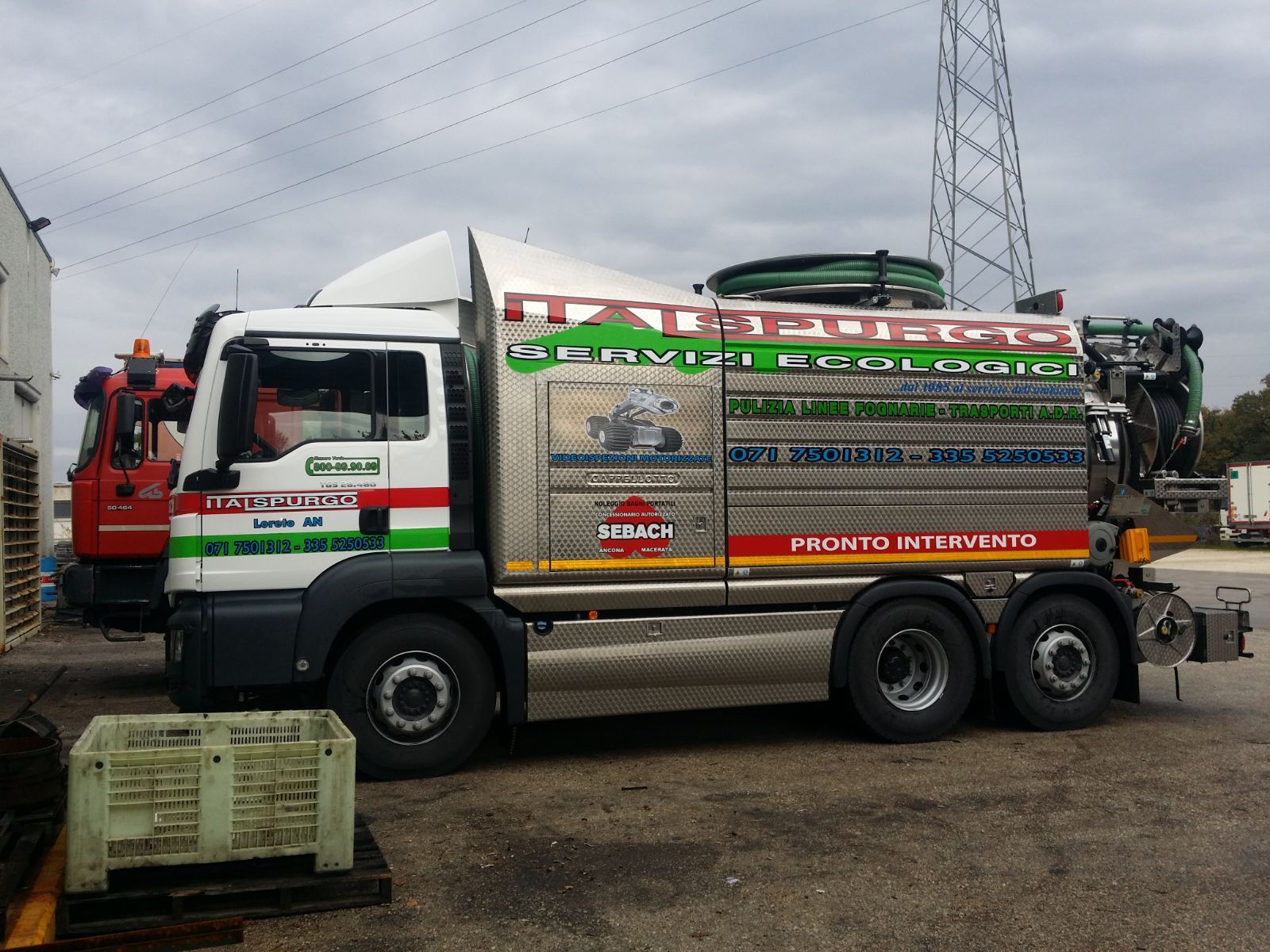 Camion di servizio rosso e bianco con serbatoio e tubi flessibili parcheggiato all'aperto su un piazzale bagnato.