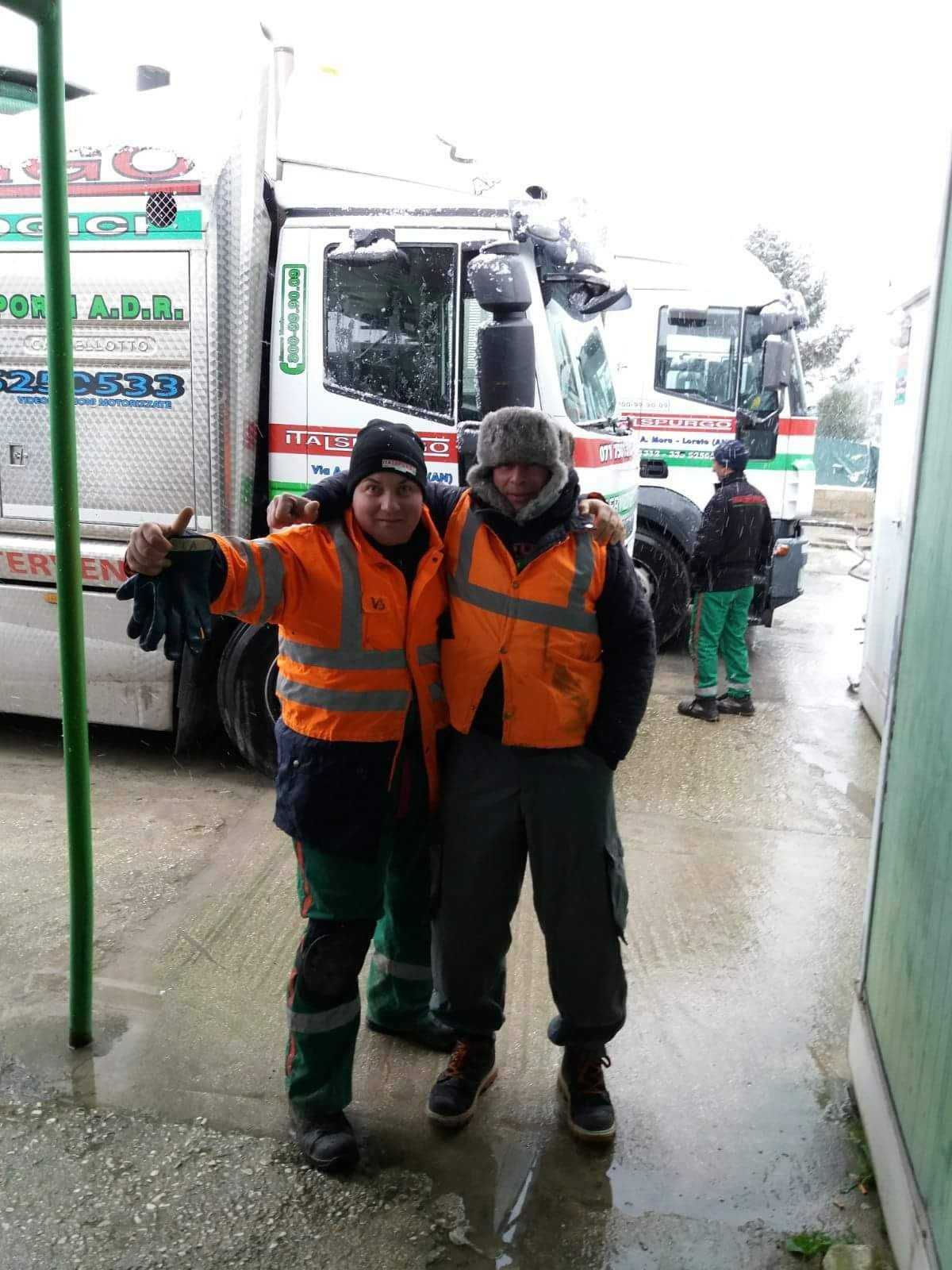 Due operai con giubbotti di sicurezza arancioni posano accanto a un camion su un marciapiede innevato.