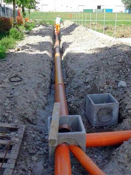 Operai che posano tubi di servizio arancioni in una trincea in un cantiere edile