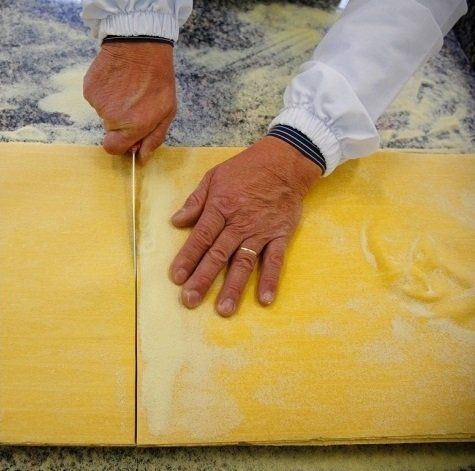 due mani di un uomo che tagliano un impasto fresco