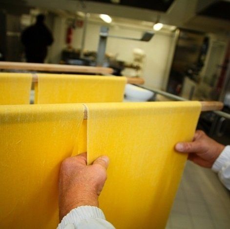 due mani di un uomo che stende delle sfoglie di pasta