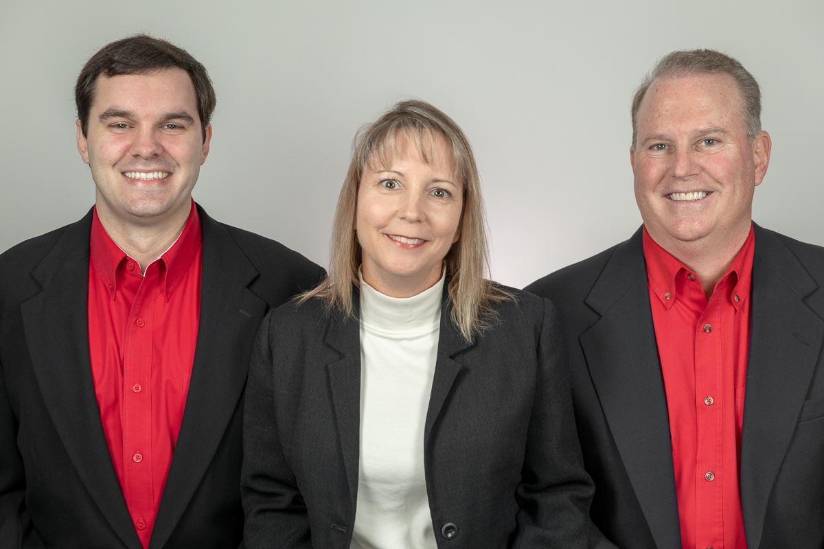 Three people in business attire smiling in front of a neutral backdrop.