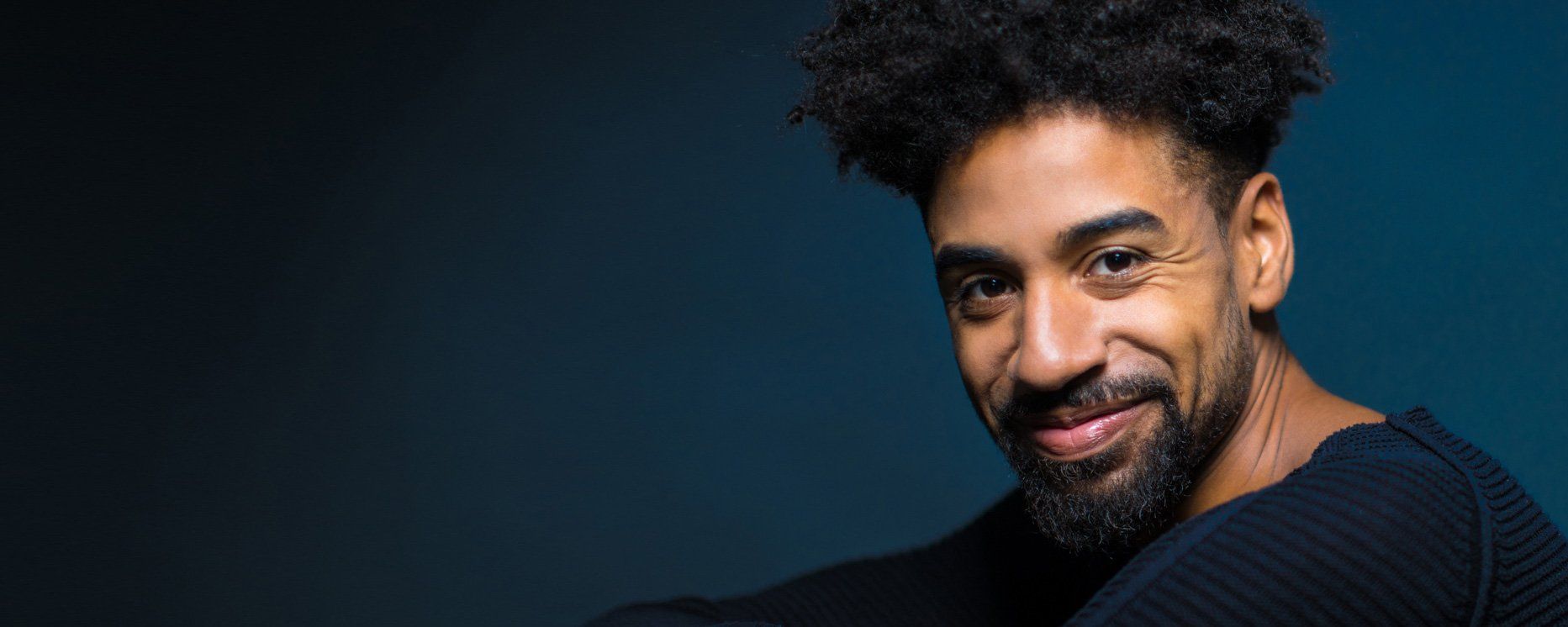 A man with a beard and curly hair is smiling for the camera.