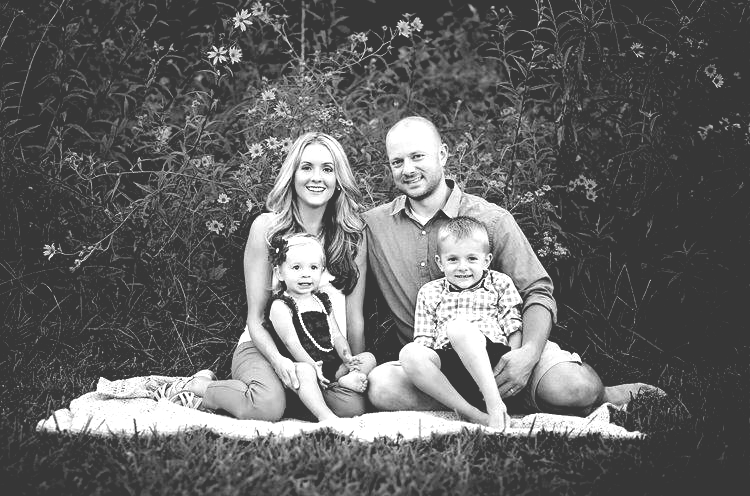 A black and white photo of a family sitting on a blanket in the grass.