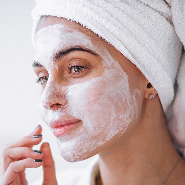 A woman with a towel wrapped around her head has a white mask on her face.