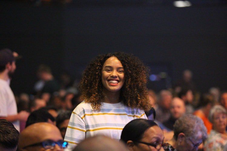 A woman is smiling in a crowd of people at a concert.