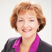Smiling woman in a dark blazer with a purple blouse against a white background
