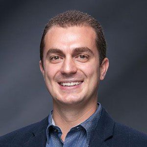 Portrait of a smiling man in a navy blazer against a dark gray background