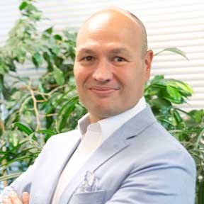 A man in a suit and tie is standing in front of a plant.
