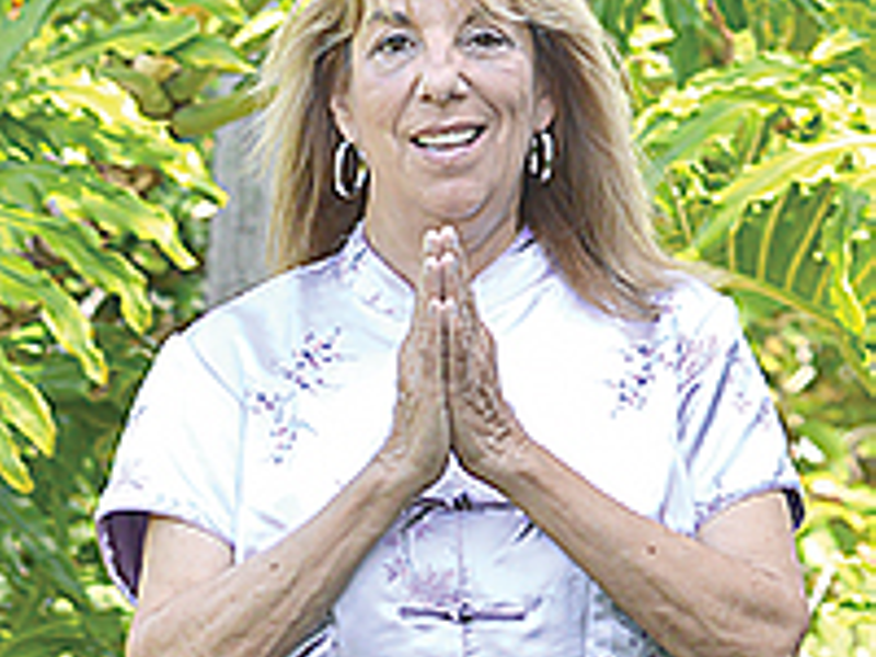 Woman in white shirt with hands pressed together, standing in front of lush green plants.