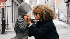 Person adjusting a child’s hood on a city street, both smiling