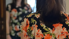 Woman in a black floral top seen from behind, with orange and white flowers in a softly blurred background