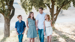 Family of four walking outdoors among trees in bright sunlight