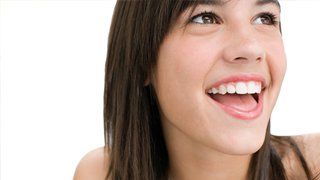 Invisalign Teen. Frau mit braunem Haar, breit lächelnd, mit strahlenden Augen nach oben blickend; weißer Hintergrund.