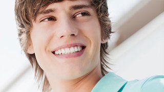 Invisalign Teen. Lächelnder junger Mann mit hellbraunem Haar, trägt ein blaues Hemd und blickt nach oben.