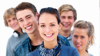 Invisalign Teen. Gruppe lächelnder junger Menschen, in der Mitte eine Frau.