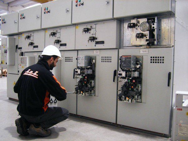 Uomo con casco al lavoro su un quadro elettrico. Armadietti grigi, al chiuso.