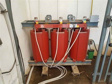 Tre trasformatori elettrici rossi montati su supporti metallici. Da ognuno partono fili bianchi.