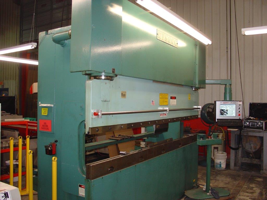 Large teal industrial press brake in a factory workshop, with a control panel and metal parts nearby