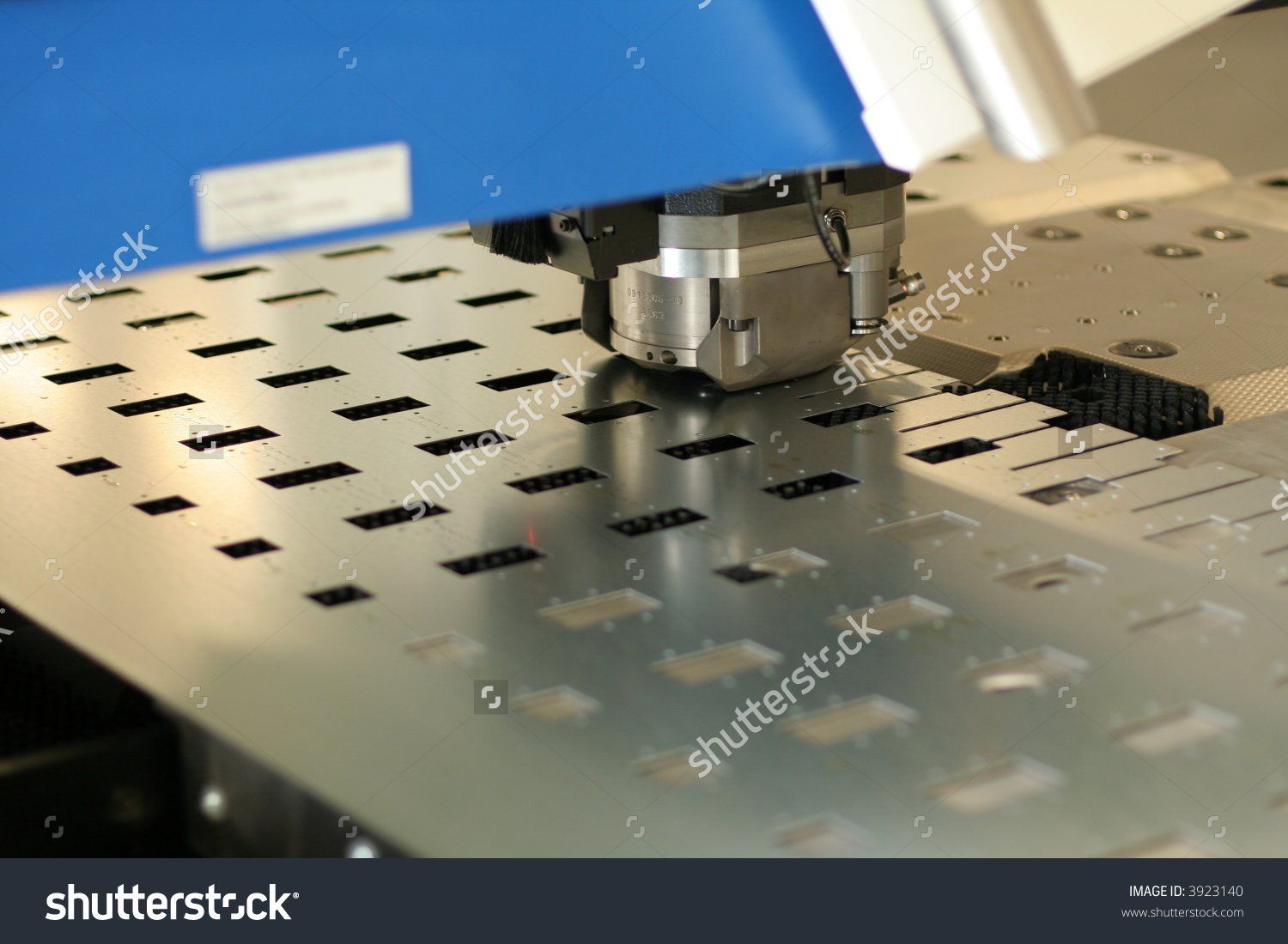 Industrial machine cutting sheet metal with rows of rectangular holes in a workshop