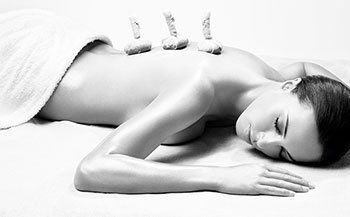 A woman is laying on a bed getting a massage with rocks on her back.