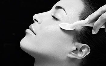 A woman is getting a facial treatment with a spoon.