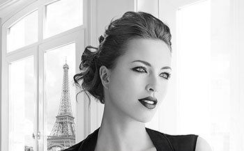 A woman is standing in front of a window with the eiffel tower in the background.